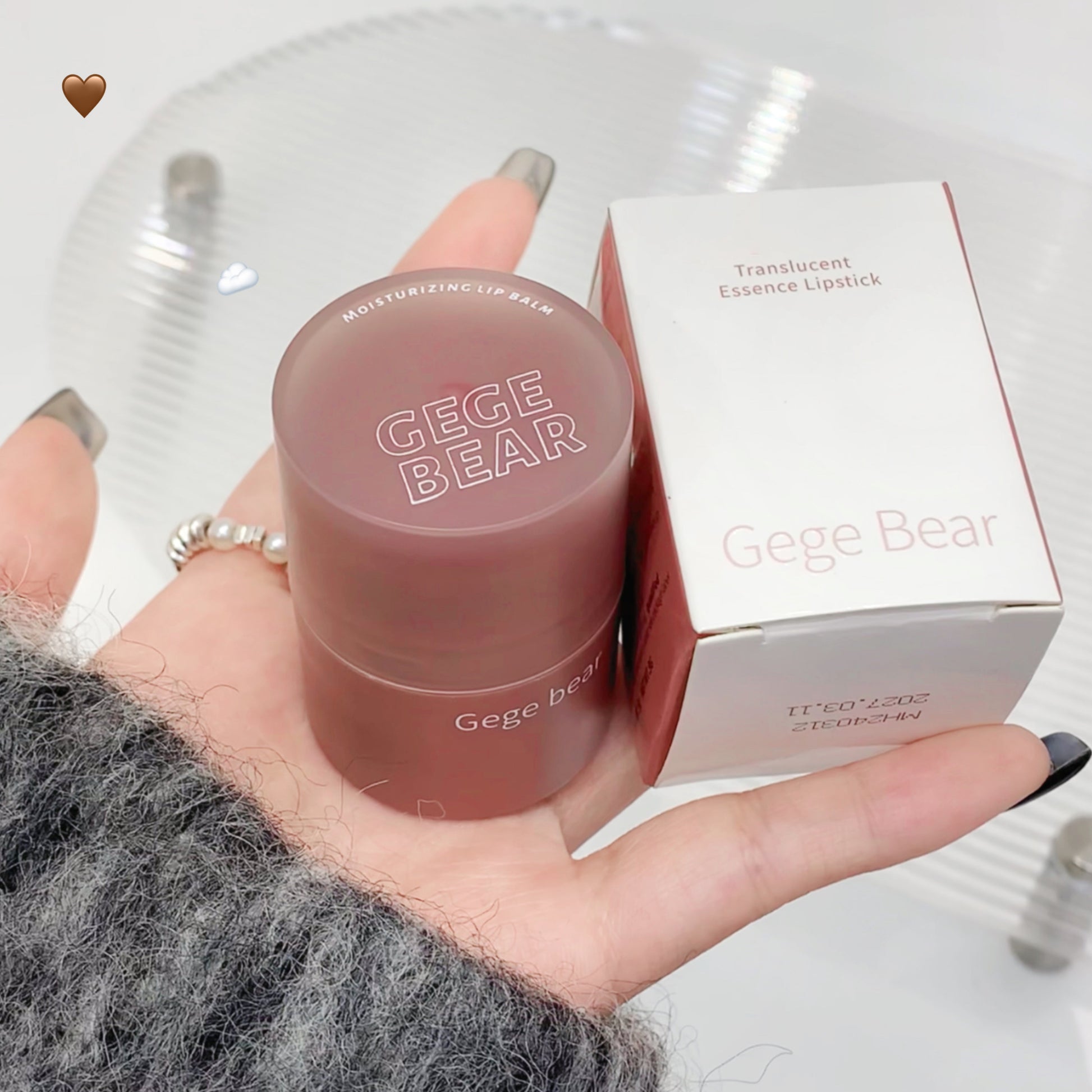 Pink lip balm with 'Gege Bear' branding held in a hand, next to its packaging.