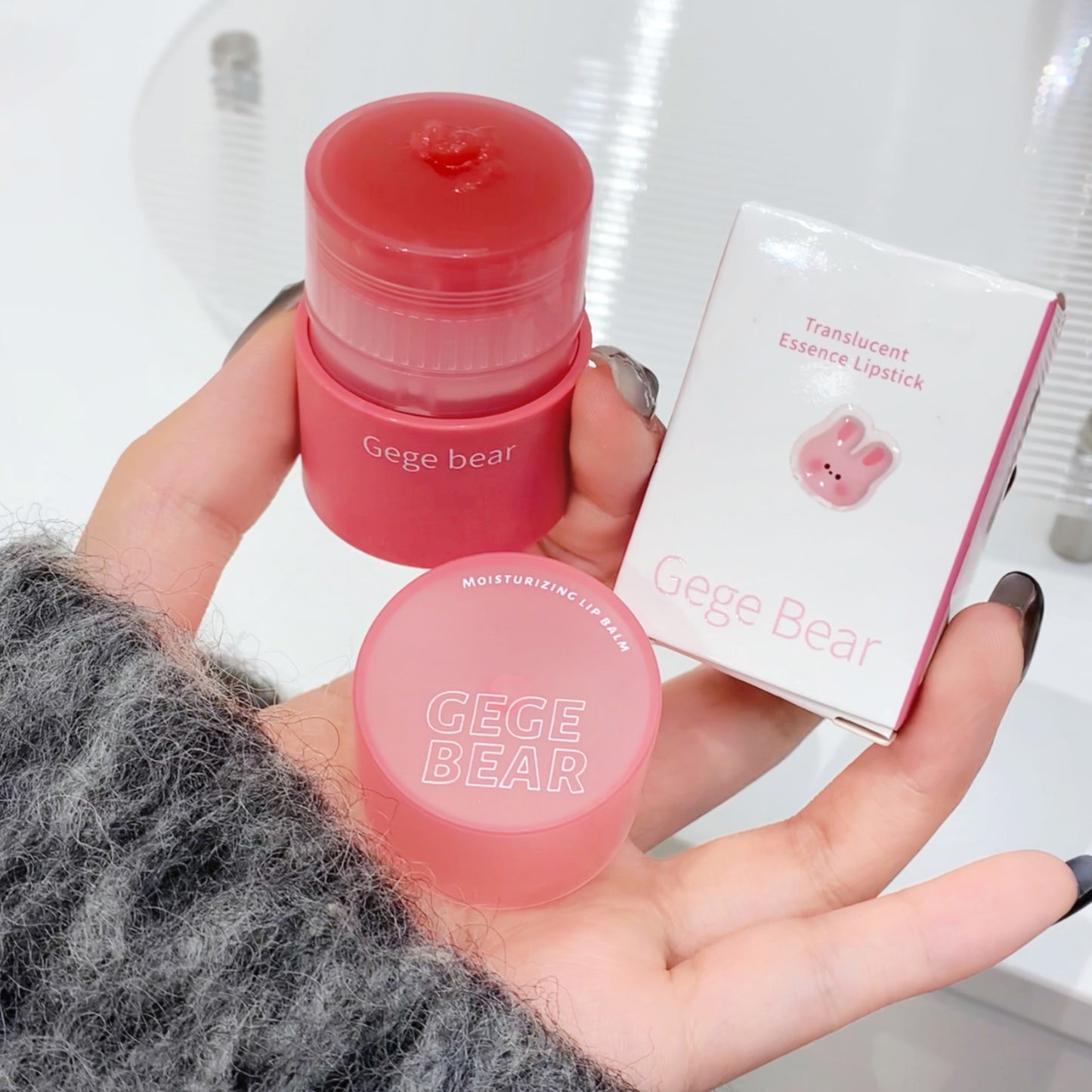 Pink Gege Bear translucent essence lipstick held in a hand with packaging in the background.