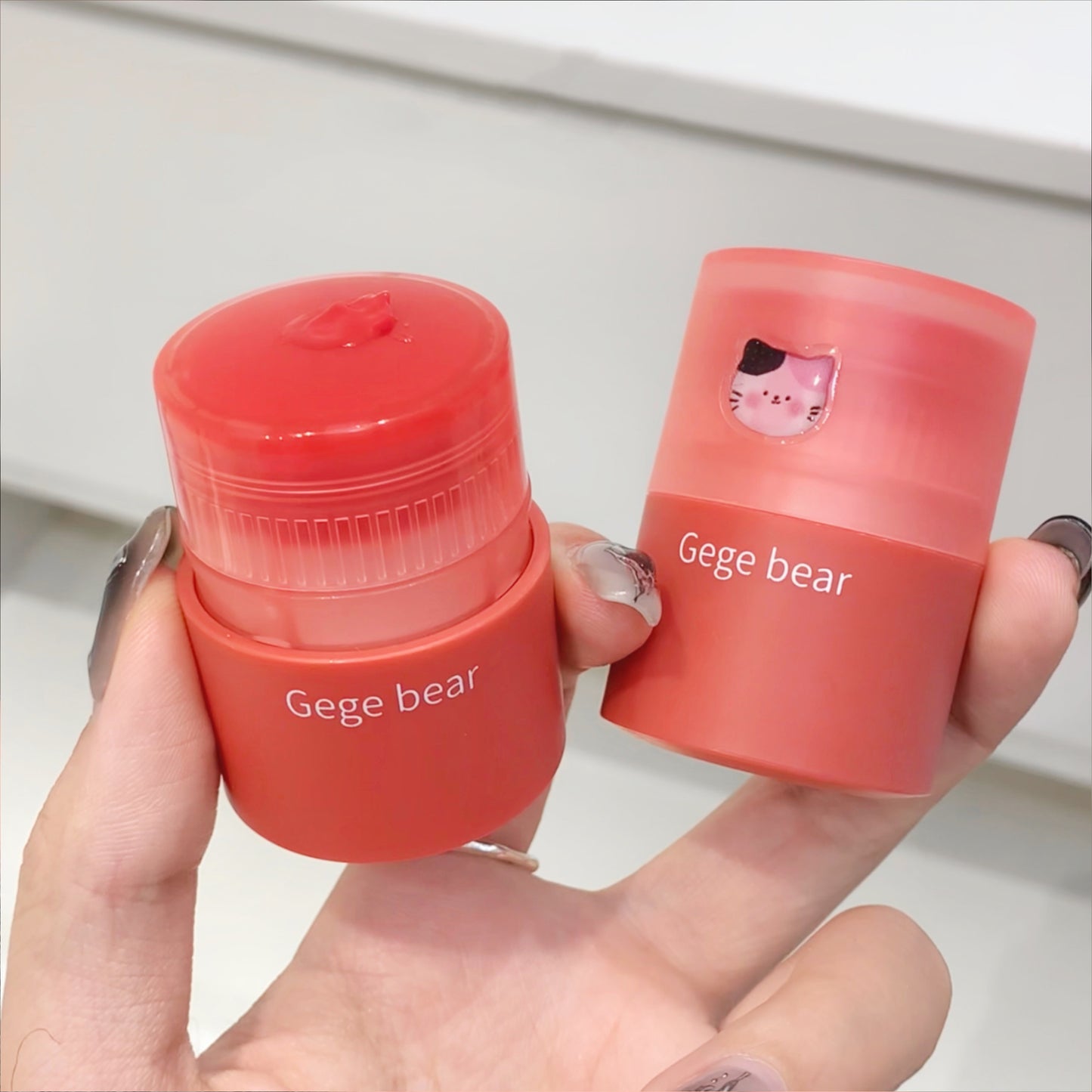 Two small red containers with 'Gege bear' branding held in a hand against a neutral background.