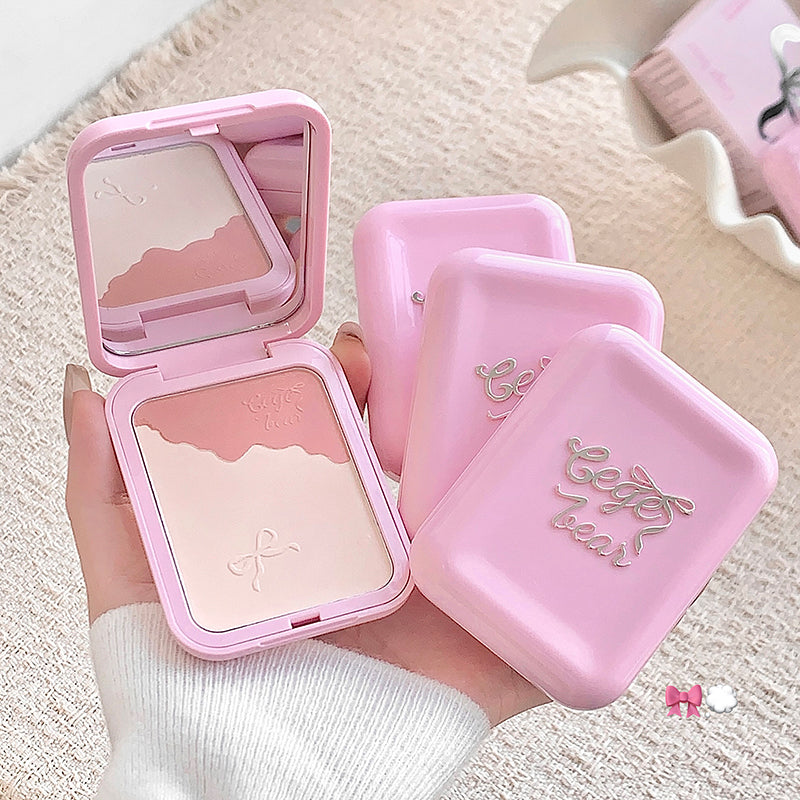 Pink makeup compact with mirror held by a hand on a light background
