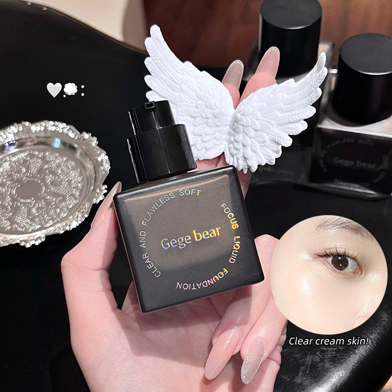 Hand holding a black makeup bottle with angel wings, surrounded by cosmetic items on a dark surface.