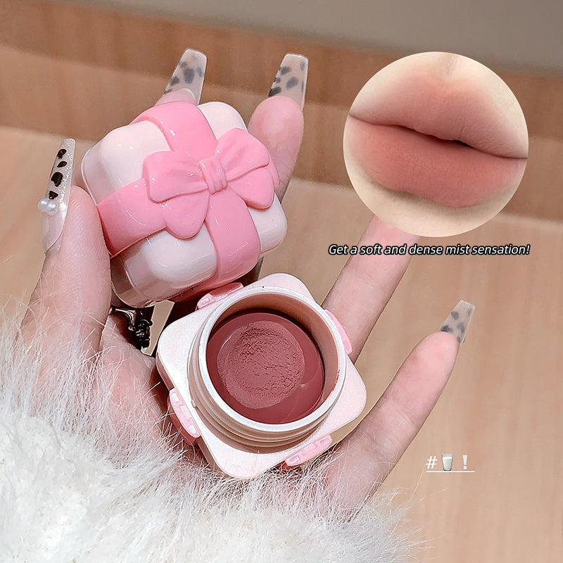 Pink makeup compact with a bow held by a hand, close-up of pink lipstick, and text on a beige background.