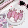 Set of pink miniature bottles on a white plate with pink sunglasses and other items in the background.
