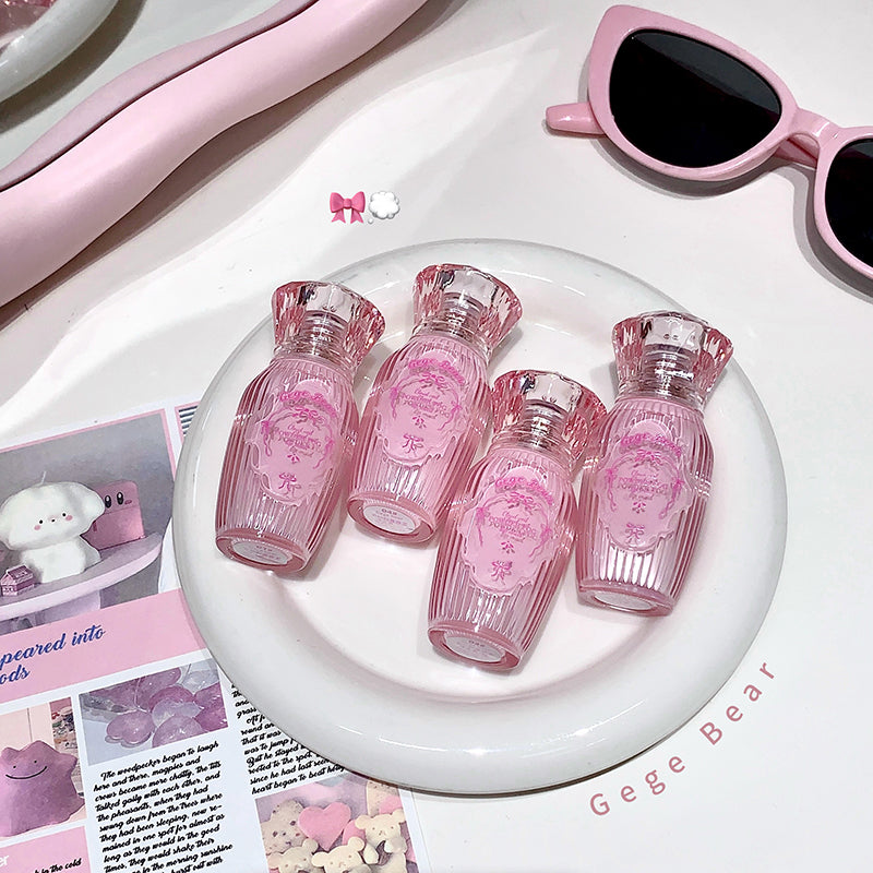 Set of pink miniature bottles on a white plate with pink sunglasses and other items in the background.