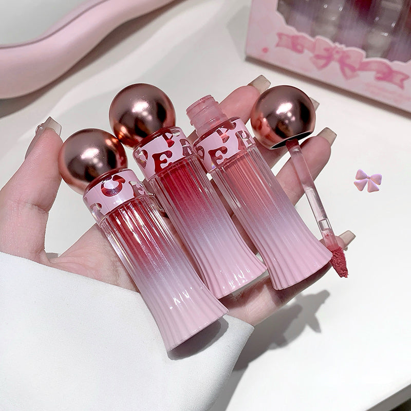 Set of pink and red gradient lip glosses with rose gold caps held by a hand.