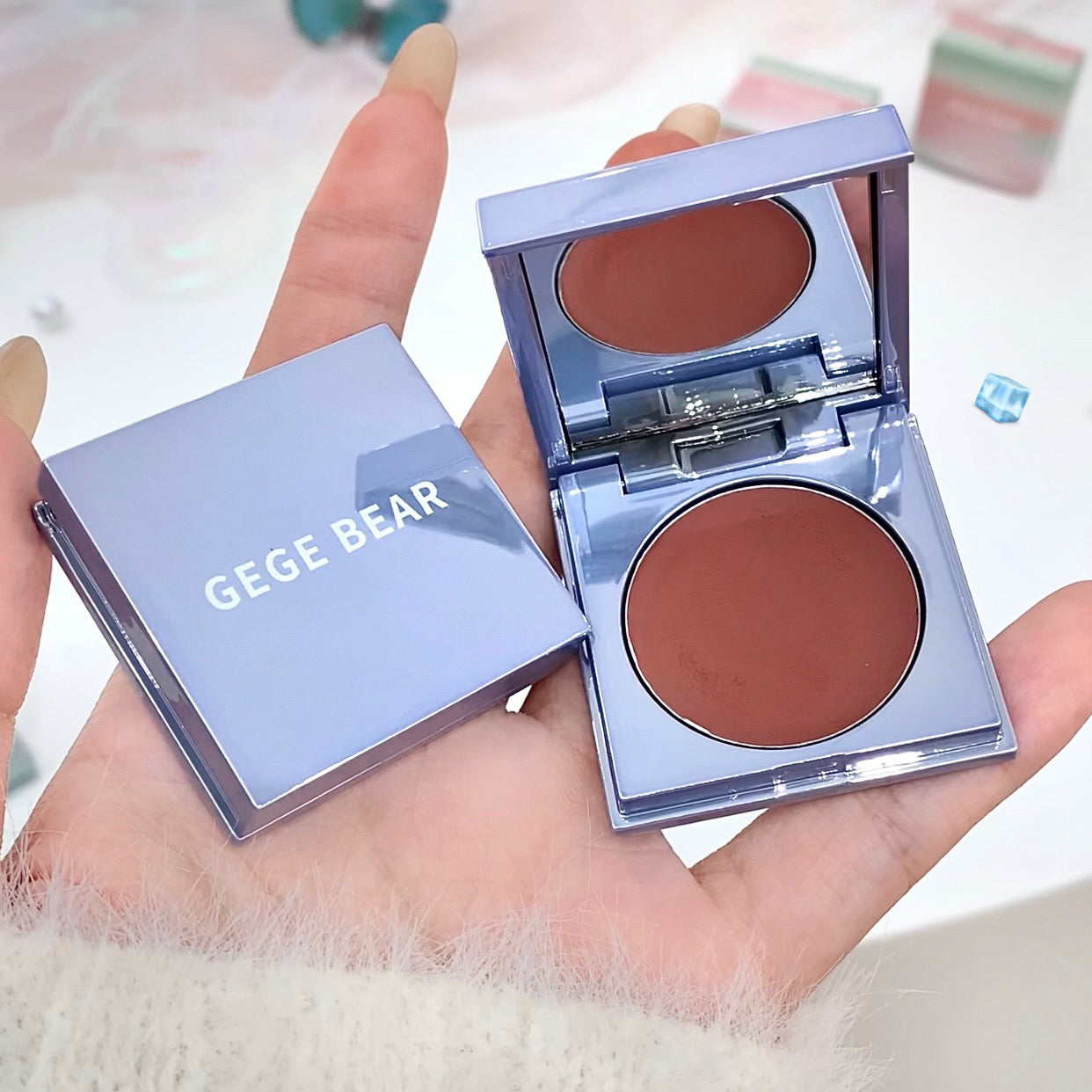 Compact blush with 'GEGE BEAR' branding held in a hand against a blurred background.