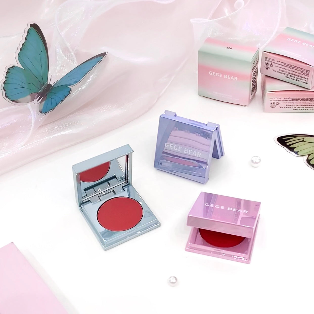 Makeup product with open case showing red color, surrounded by closed cases and boxes on a light pink background.