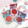 Three compact blushes in different colors held by a hand on a light background