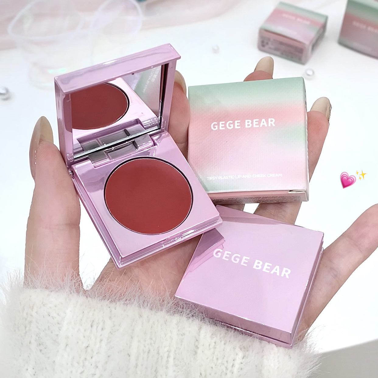 Pink blush compact with mirror and 'GEGE BEAR' packaging held by a hand.
