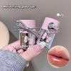 Two small glass lip glosses with pink caps held by a hand, showing a close-up of glossy lips.