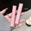 Two pink lip glosses held by a hand with a black background