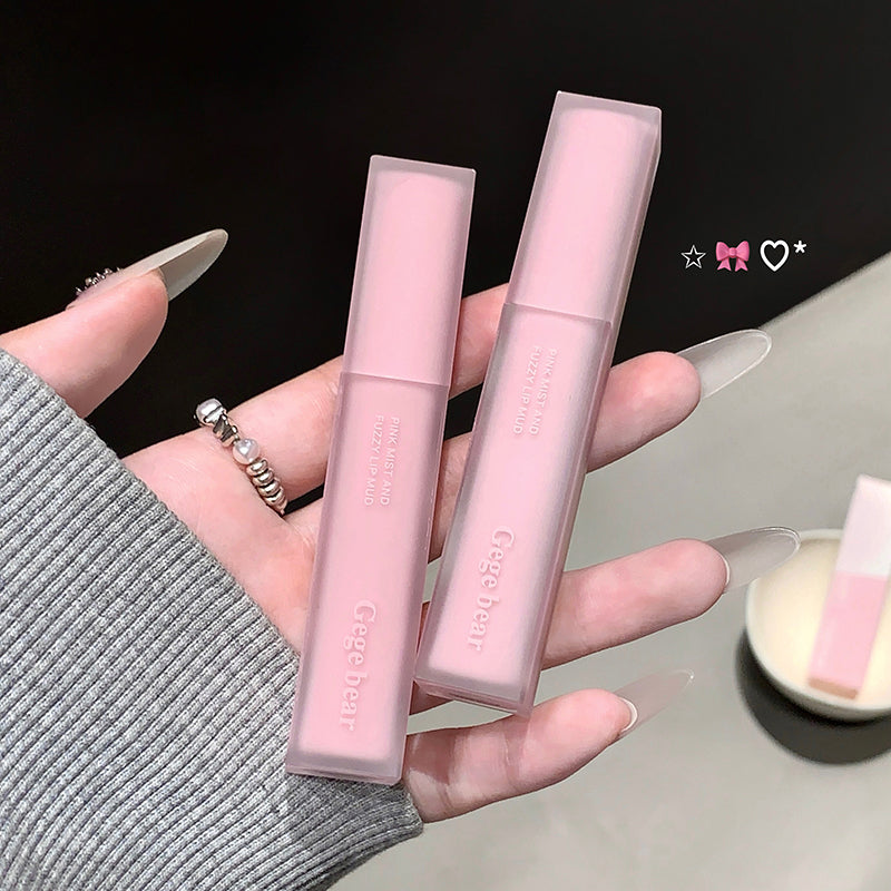 Two pink lip glosses held by a hand with a black background