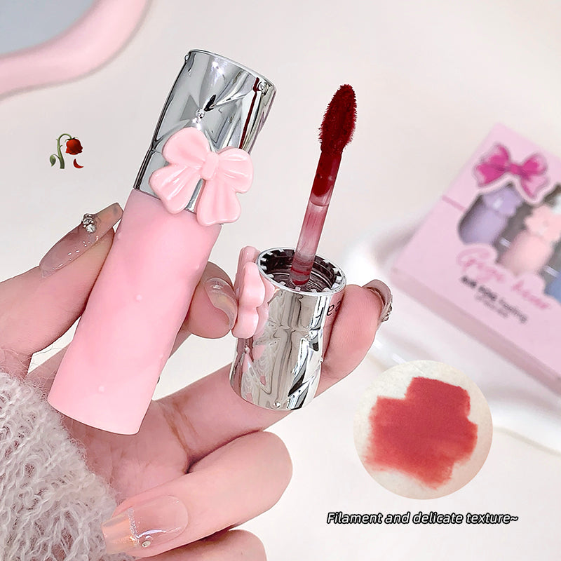 Pink lip gloss with silver cap held by a hand, close-up on a light background.