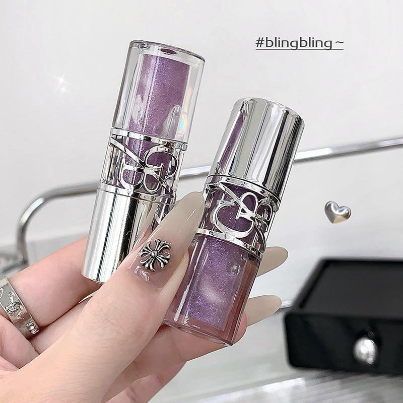 Purple lip gloss with silver cap held by a hand, blurred background