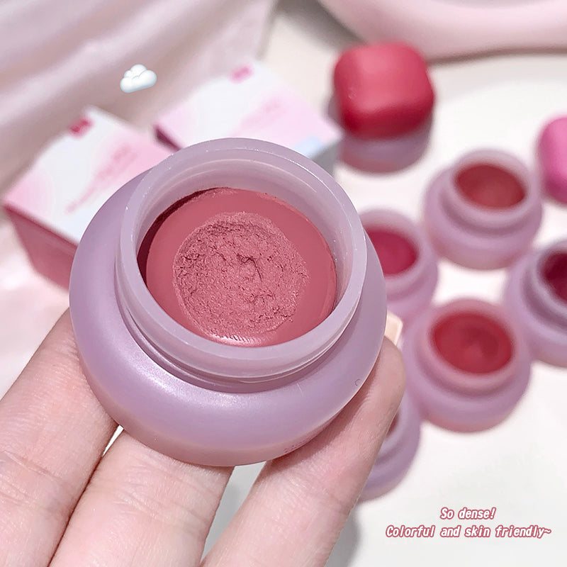 Pink lip balm container held by a hand with more lip balms in the background.