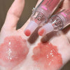Two lip glosses being applied to a hand with visible gloss on skin.