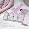Set of GEUGE BEAR bottles with pink caps on a white surface, with packaging and a cherry in the background.