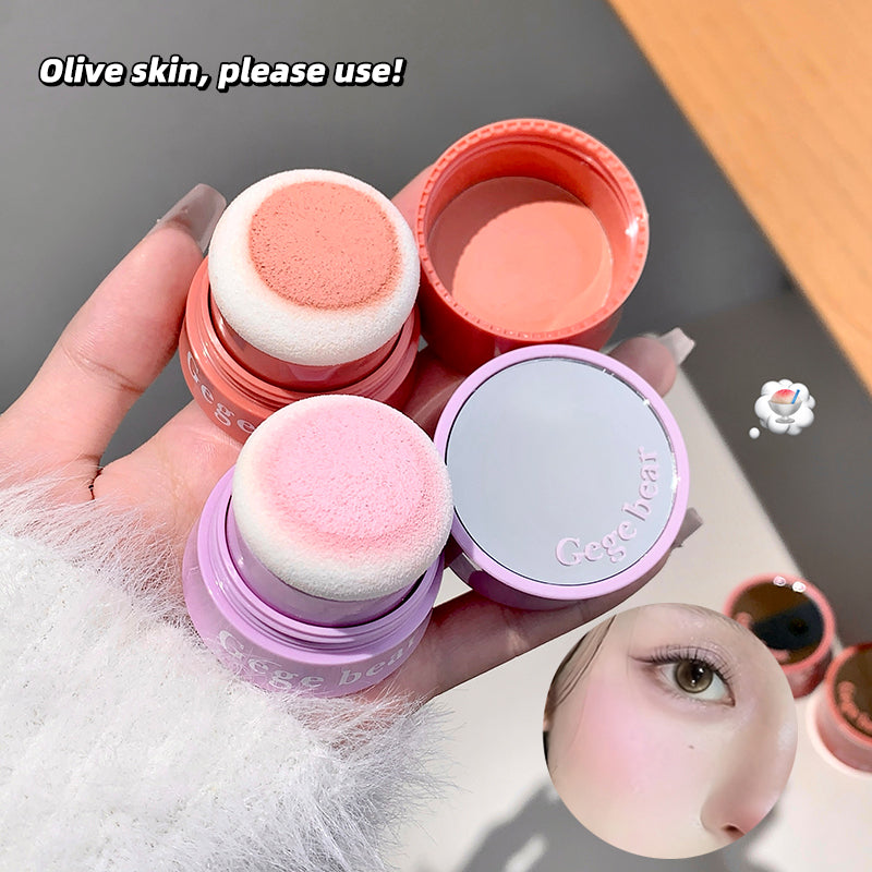 Three makeup sponges in different colors held by a hand, with a blurred background.