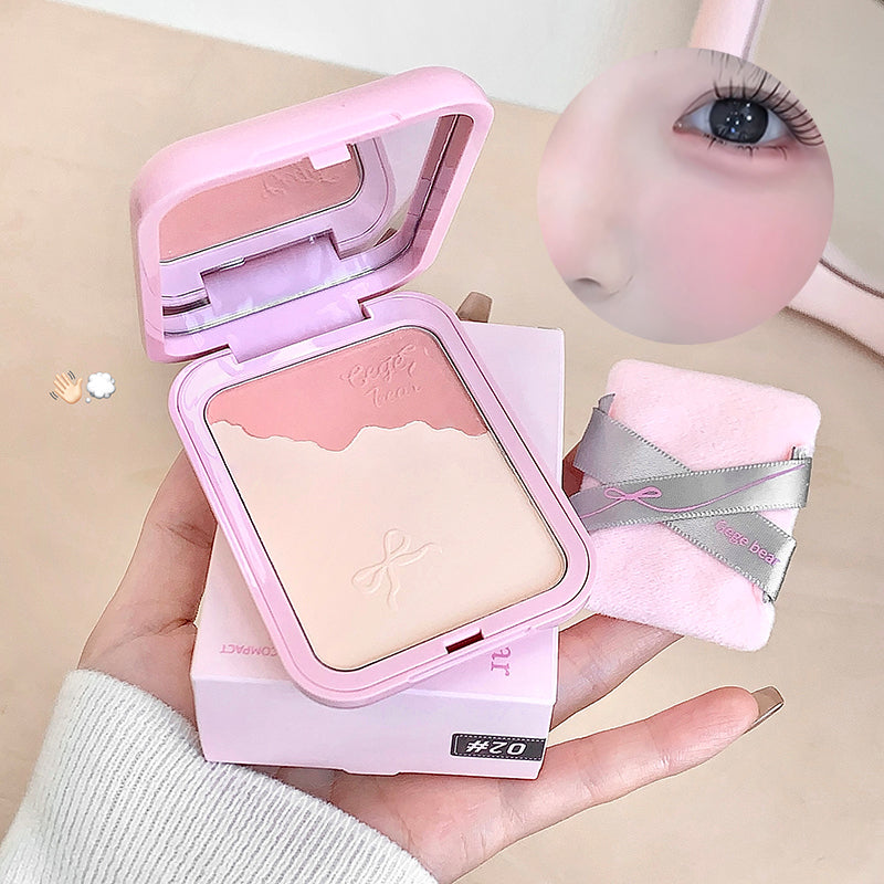 Pink makeup compact held in a hand with a blurred eye and brush in the background