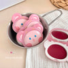 Pink bear-shaped blushes in a metal container on a beige surface.