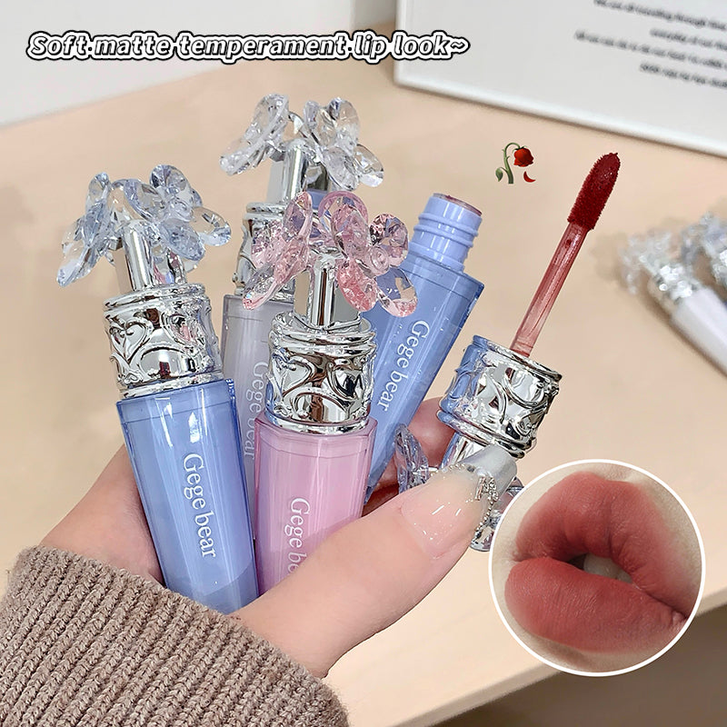 Set of lip glosses with decorative caps held by a hand, close-up of lips shown.
