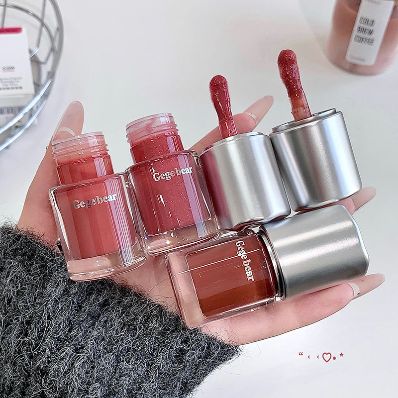 Hand holding multiple lip glosses with visible brand name 'Cdegear' on a neutral background.