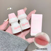 Two small white bottles with pink caps held by a hand, next to a pink box, on a neutral background.