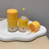 Two yellow skincare products with a third one open on a white surface against a gray background