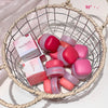 Pink and red lip balm containers and boxes in a wire basket on a light background