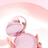 Pink makeup compact held by a hand with a soft pink background