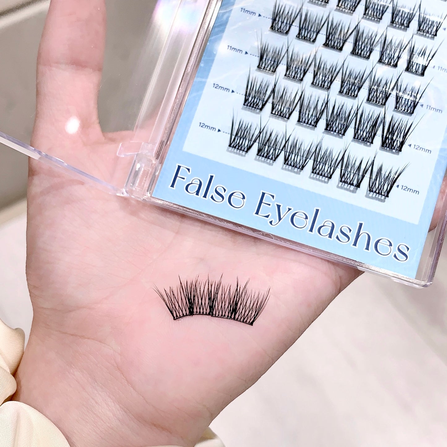 False eyelashes on a hand with packaging labeled 'False Eyelashes' in the background.