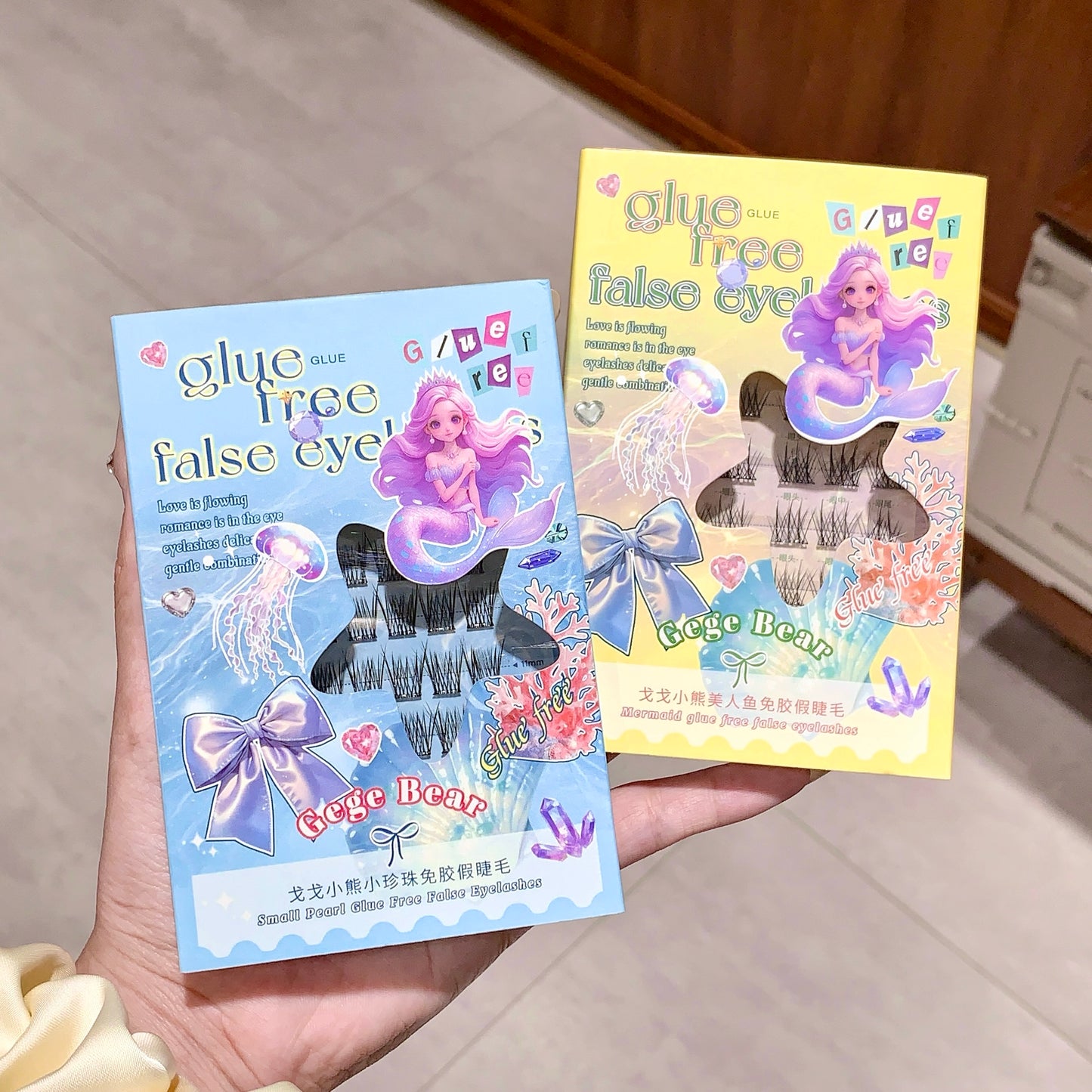 Two packages of glue-free false eyelashes with mermaid design packaging held by a hand.