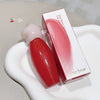 Red lip gloss with pink cap on a white surface, accompanied by its packaging.