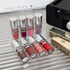 Set of lip glosses with a GEUGE BEAR branded box on a reflective surface.