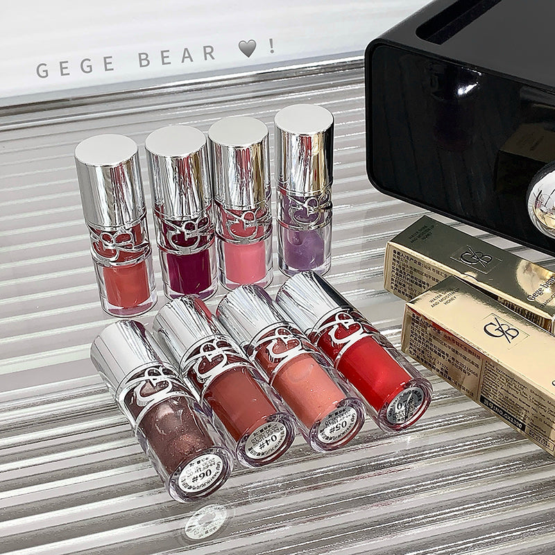 Set of lip glosses with a GEUGE BEAR branded box on a reflective surface.