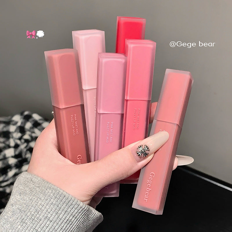 Hand holding multiple pink lip glosses with visible brand name on a neutral background