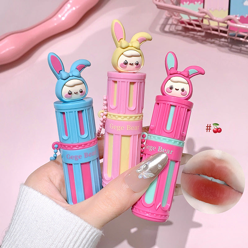 Three colorful lip balms with cartoon character designs held by a hand against a pink background.