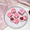 Pink floral lip balm containers on a white plate with a pink box in the background.