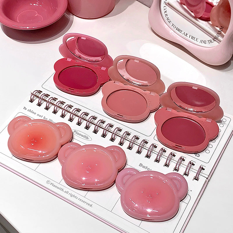Pink makeup products on a white surface with a notebook