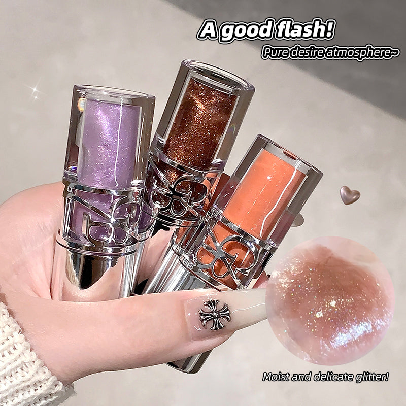 Three lip glosses in purple, gold, and orange held by a hand with a decorative nail design.