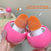 Two orange makeup brushes with pink handles held by a hand against a neutral background.