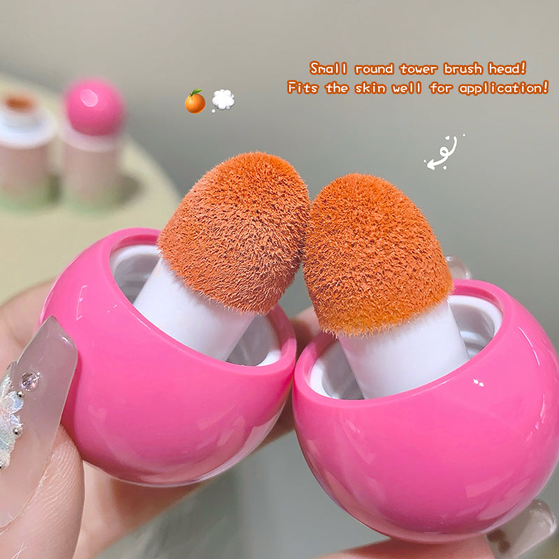 Two orange makeup brushes with pink handles held by a hand against a neutral background.
