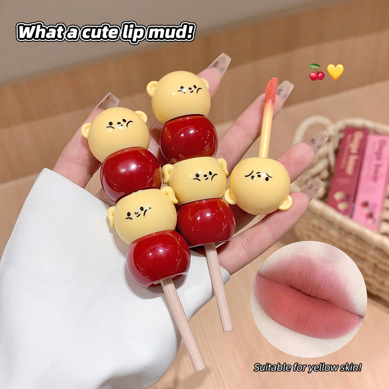 Lip mud on a stick with bear and cherry design held by a hand, with text 'What a cute lip mud!' and 'Suitable for yellow skin!'.