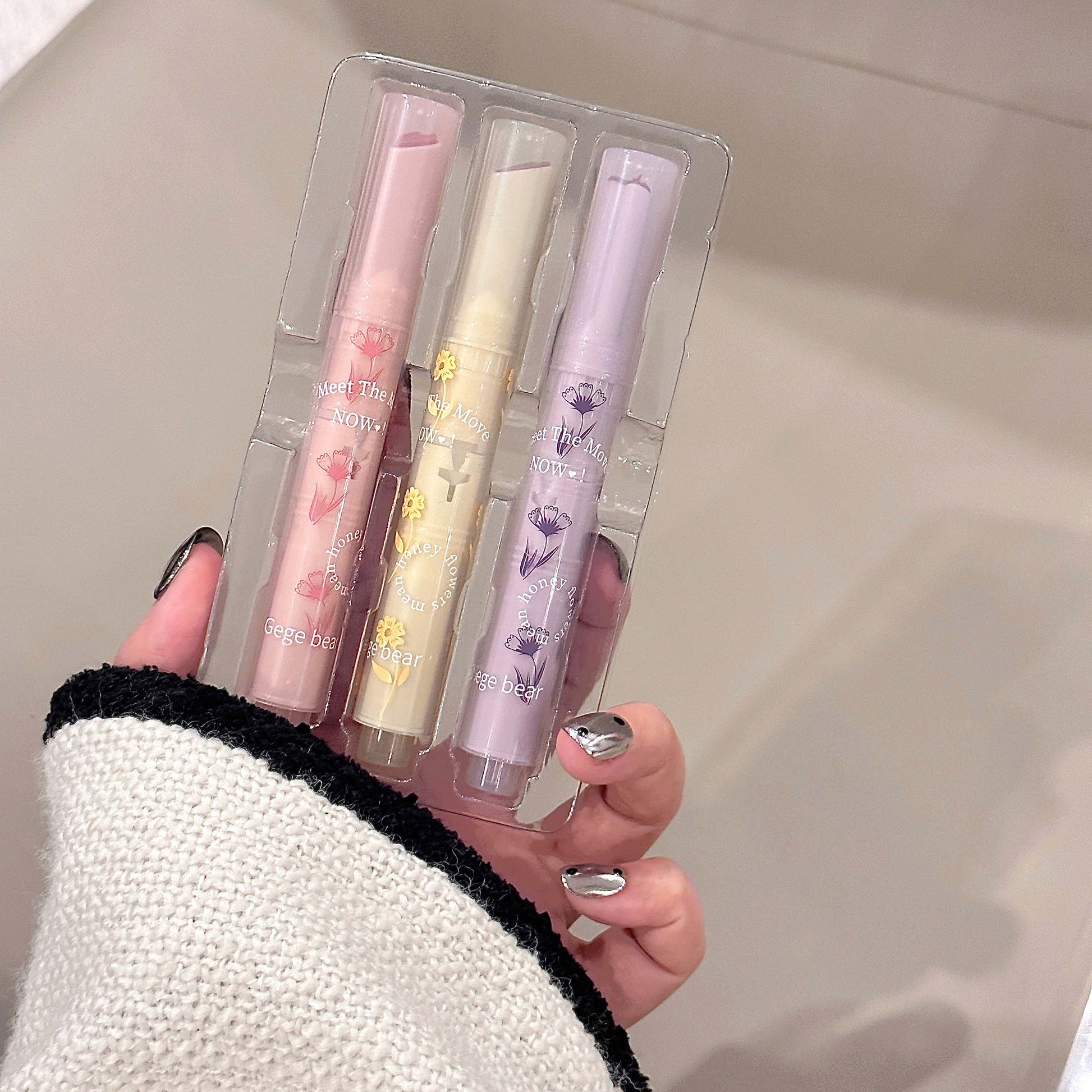 Four lip glosses in clear packaging held by a person with a neutral background