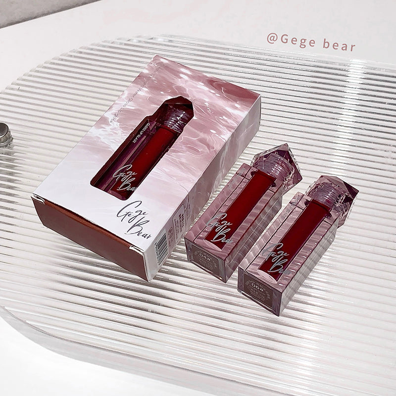 Red lip gloss with packaging on a textured white surface, branded 'Gege bear'.