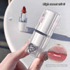 Lipstick with decorative heart design held by a hand, on a light background.