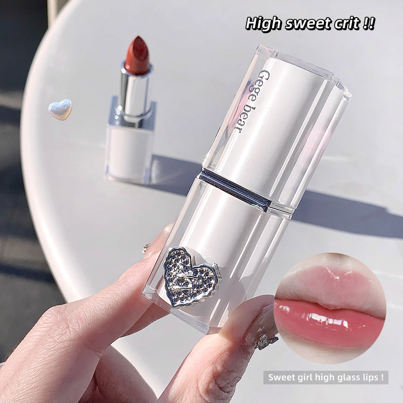 Lipstick with decorative heart design held by a hand, on a light background.