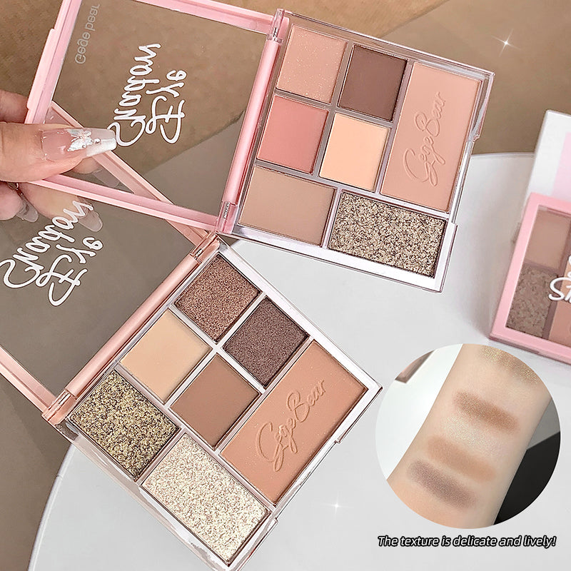 Makeup palette with various shades of eyeshadows and a hand holding it.