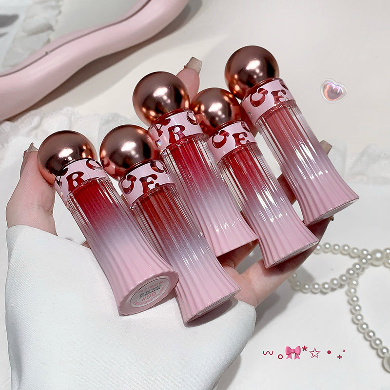 Set of pink and red lip glosses with metallic tops held by a hand.