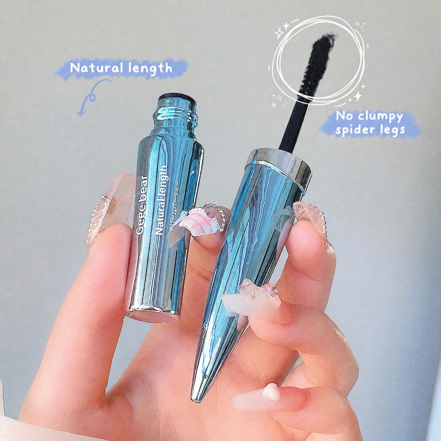 Blue mascara with silver cap held by a hand against a gray background